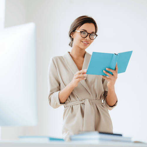 A business-professional women standing while reading a blue planner